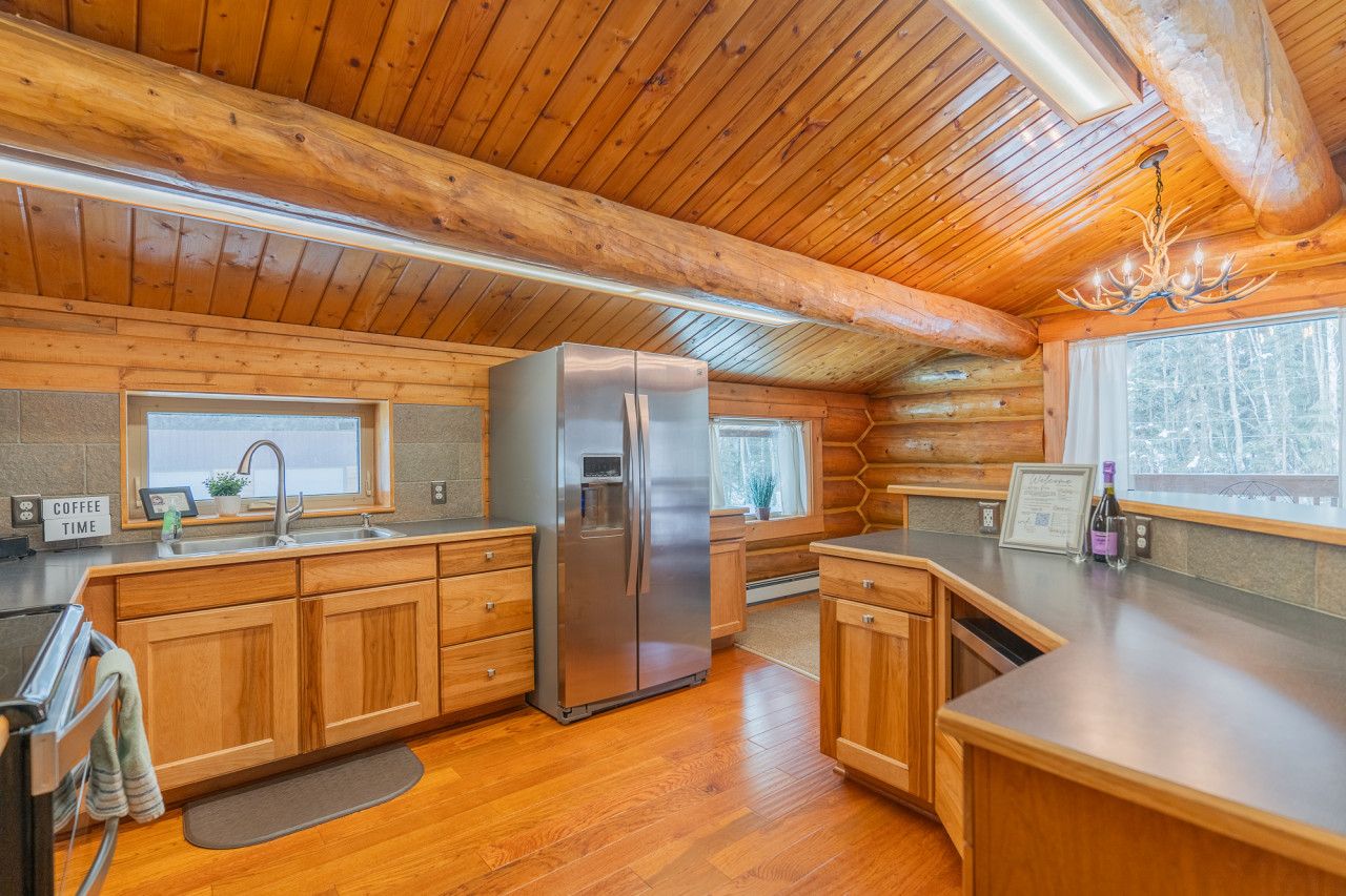 A log cabin interior with a kitchen featuring wooden cabinets, a stainless steel refrigerator, and a chandelier.
