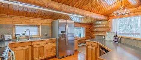 A log cabin interior with a kitchen featuring wooden cabinets, a stainless steel refrigerator, and a chandelier.