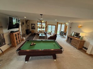 Une table de billard dans une pièce dotée d’une cheminée en pierre, d’un téléviseur et d’un coin repas.