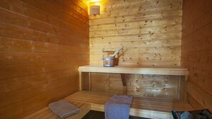 Een sauna met houten wanden, een bank, een zitbank, een handdoek en een emmer.