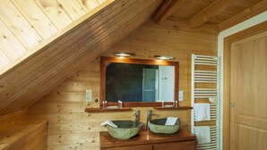 Een houten badkamer met twee stenen wastafels, een spiegel en een handdoekrek.