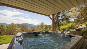 Een hottub onder een houten pergola, omgeven door weelderige begroeiing en een bergachtig landschap.