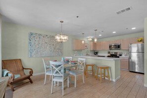 A modern kitchen with a central island, wooden cabinets, stainless steel appliances, and a dining area with a glass table and chairs.