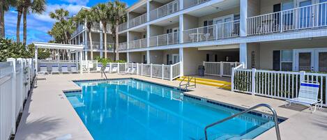A pool area with a clear blue pool, white railings, and a multi-story building with balconies.