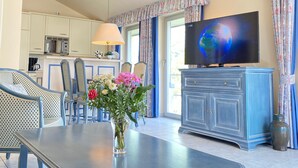 Een woonkamer met een eettafel, stoelen, een televisie en een kast.