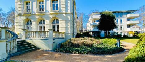 A historic building with a grand entrance, a staircase, and a well-maintained garden.