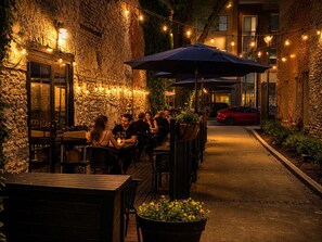 An outdoor dining area with stone walls, tables, chairs, and string lights. - Lakefront Condo On The Water W/ Exceptional Views (Sandusky)
