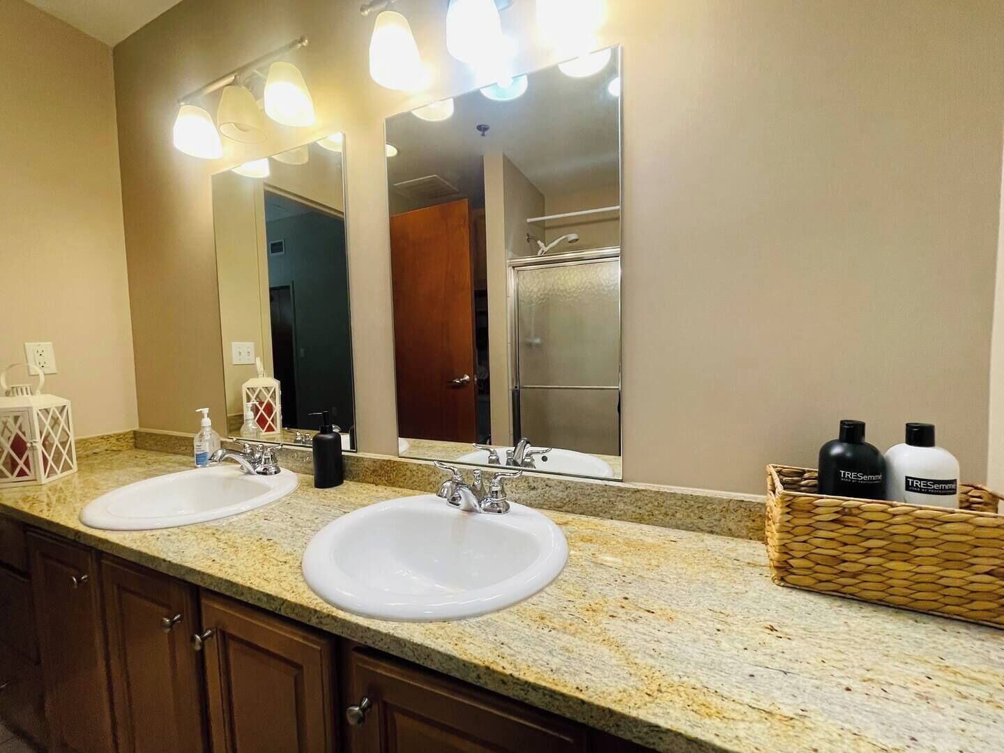Une salle de bain avec deux lavabos, un grand miroir et un panier en osier contenant des articles de toilette.