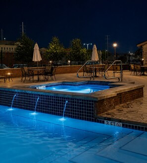 A swimming pool with a tiled edge, a lounge area with chairs and umbrellas, and a brick wall. - Lakefront Condo On The Water W/ Exceptional Views (Sandusky)