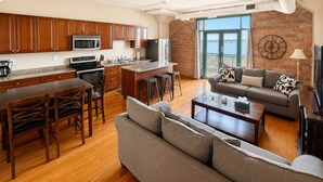 A modern kitchen with wooden cabinets, a microwave, and a refrigerator. There is a dining area with a table and chairs, and a living room with a sofa and a coffee table.