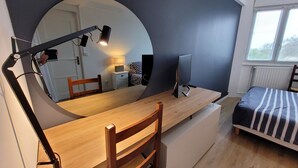 Une chambre à coucher avec un lit, un bureau avec un ordinateur, un miroir et une fenêtre.