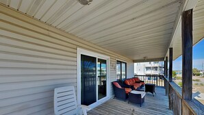 Een overdekt terras met een witte stoel, een bank met rode kussens en een houten terras.