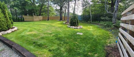 A well-maintained grassy yard with a wooden fence, a small tree, and a stone border.