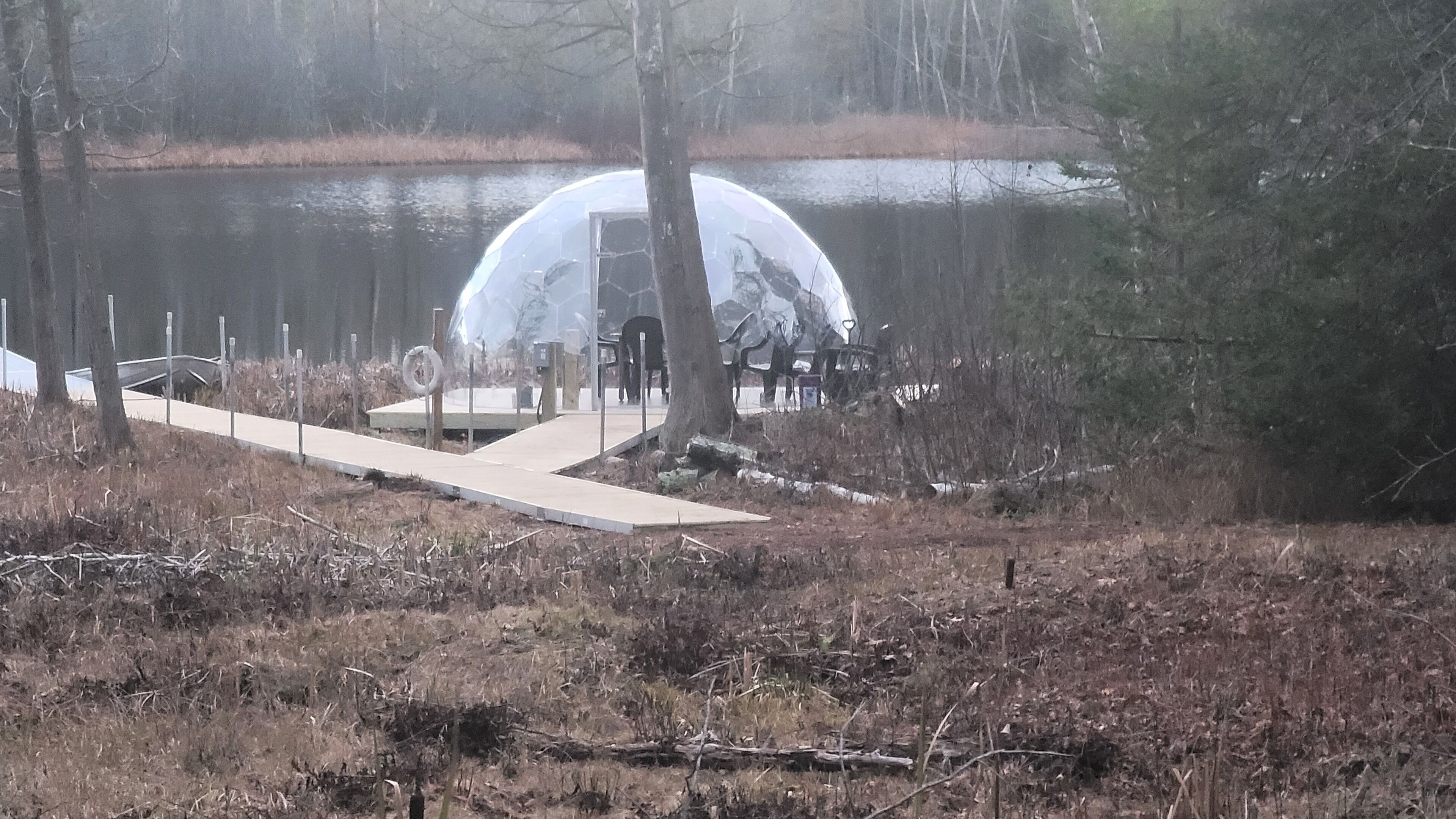A transparent dome structure over a body of water, surrounded by trees and a concrete pathway.