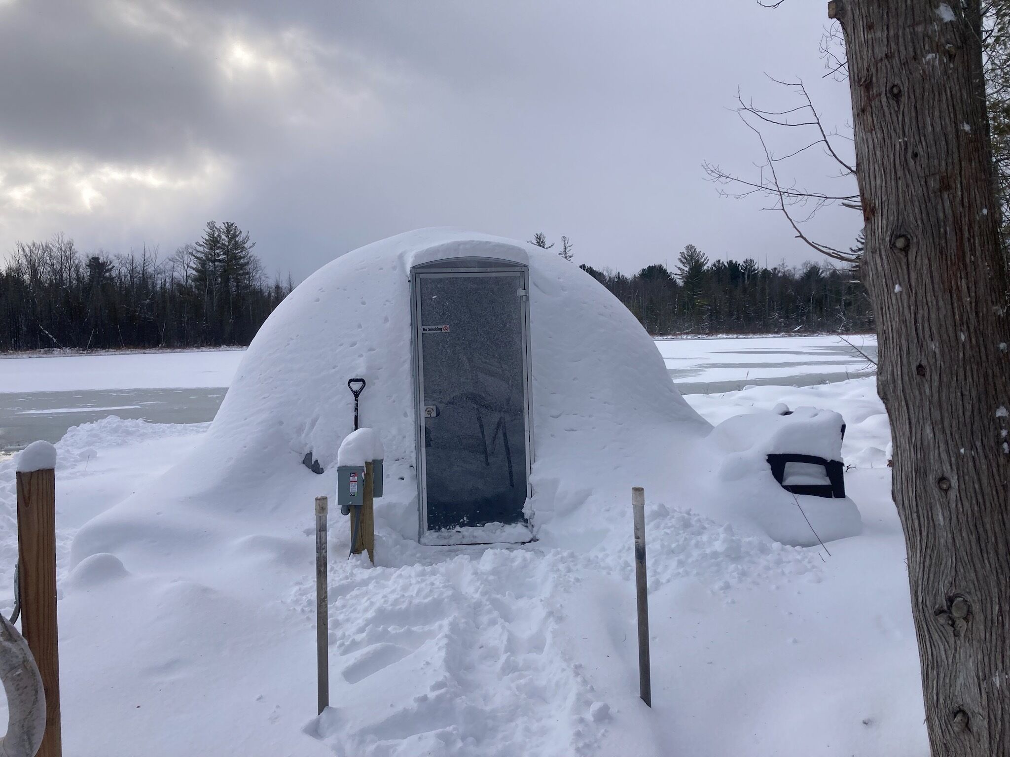 A snow-covered igloo with a door, surrounded by snow and trees.