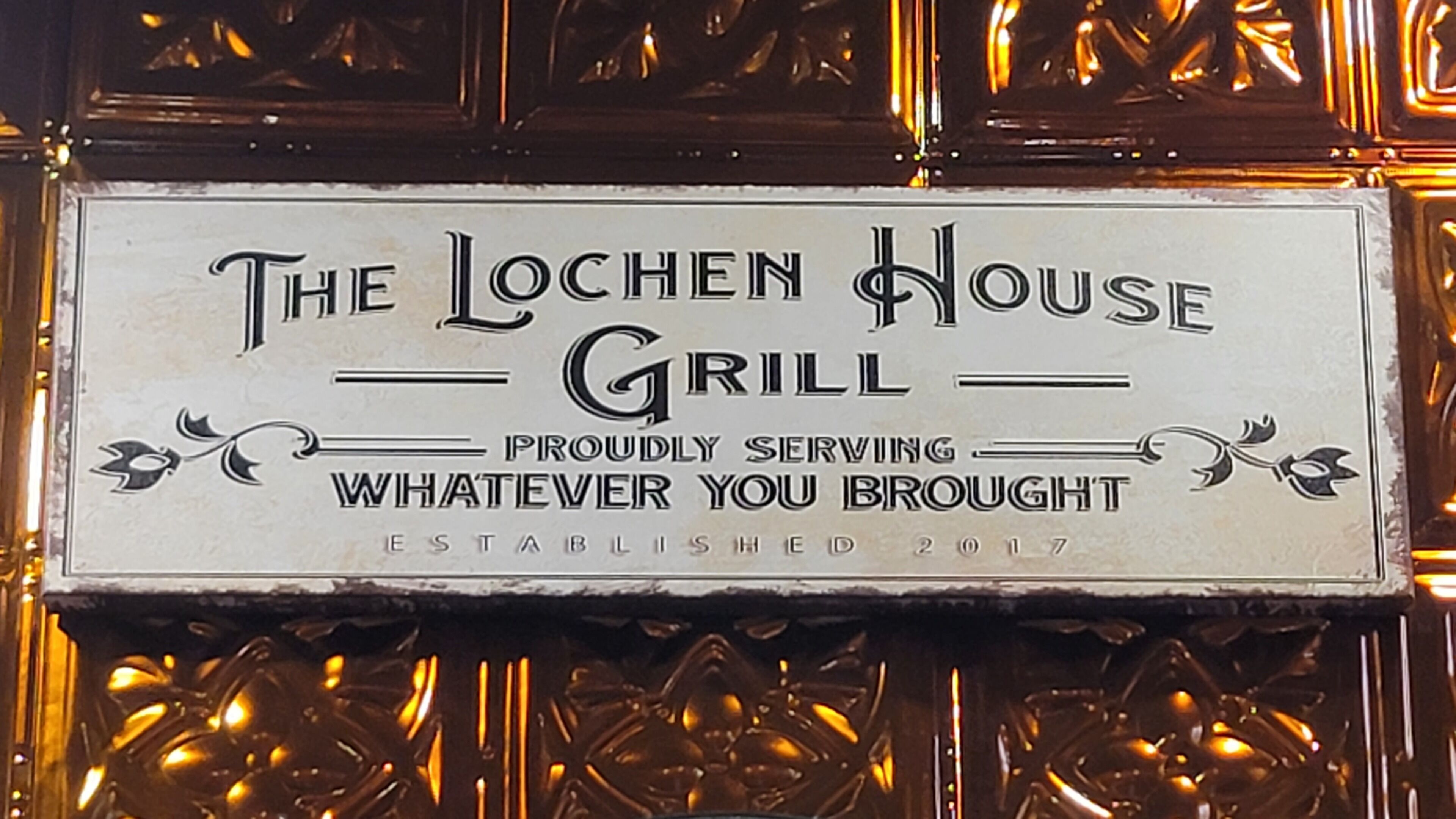 Segnale per The Lochen House Grill, fondato nel 2017, con lo slogan 'Serviamo volentieri ciò che porti'.