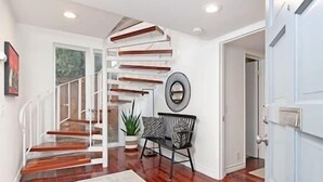 Un interior moderno con una escalera espiral, una zona de estar con una butaca estampada y una gran obra de arte abstracta en la pared.