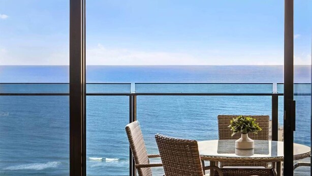 A balcony with wicker chairs and a table, overlooking a calm sea. - Sealuxe Seaview Suites - Central Surfers Paradise (Surfers Paradise)