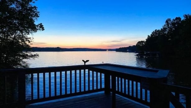 Una terraza de madera con barandilla que da a una masa de agua tranquila al atardecer.