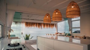 A modern kitchen with a large island, a gas stove, and a view of the ocean through large windows. - Mahi Mahi Villa & Suites (Pecatu)