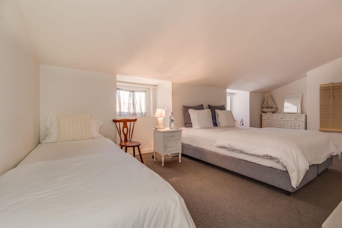 A bedroom with two beds, a nightstand, a chair, and a window with curtains.