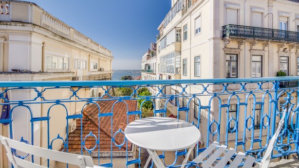 A balcony with a white table and chairs, overlooking a coastal cityscape with historic buildings. - Chiado 44 (Lisbon)