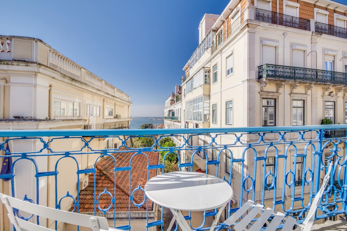 A balcony with a white table and chairs, overlooking a coastal cityscape with historic buildings.