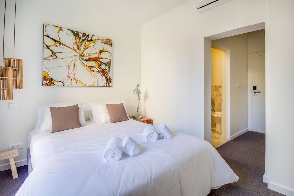 A hotel room with a large bed, a wall art piece, a bedside lamp, and a view of the bathroom.