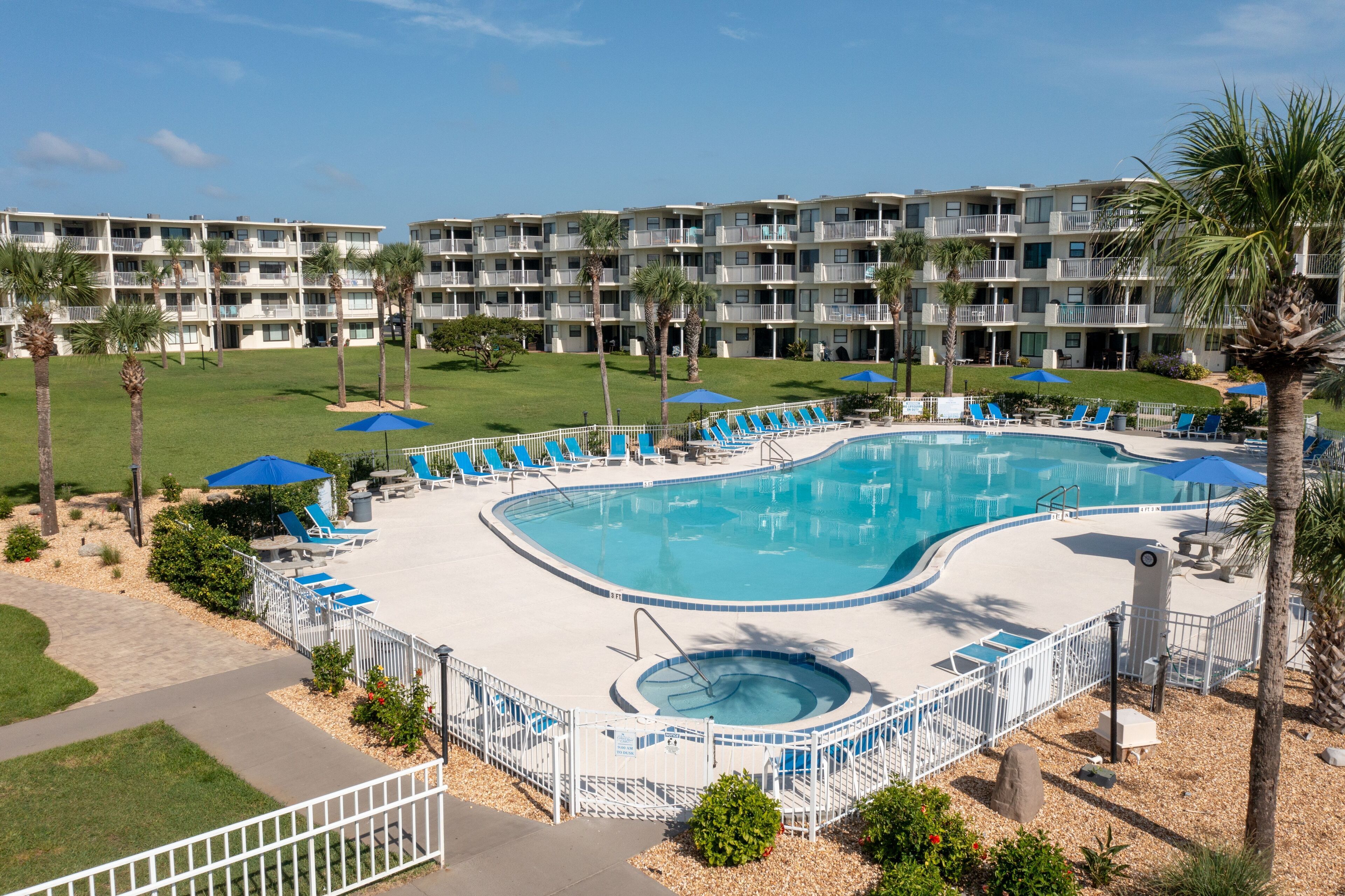 A hotel with a large pool area, multiple balconies, and a well-maintained lawn.