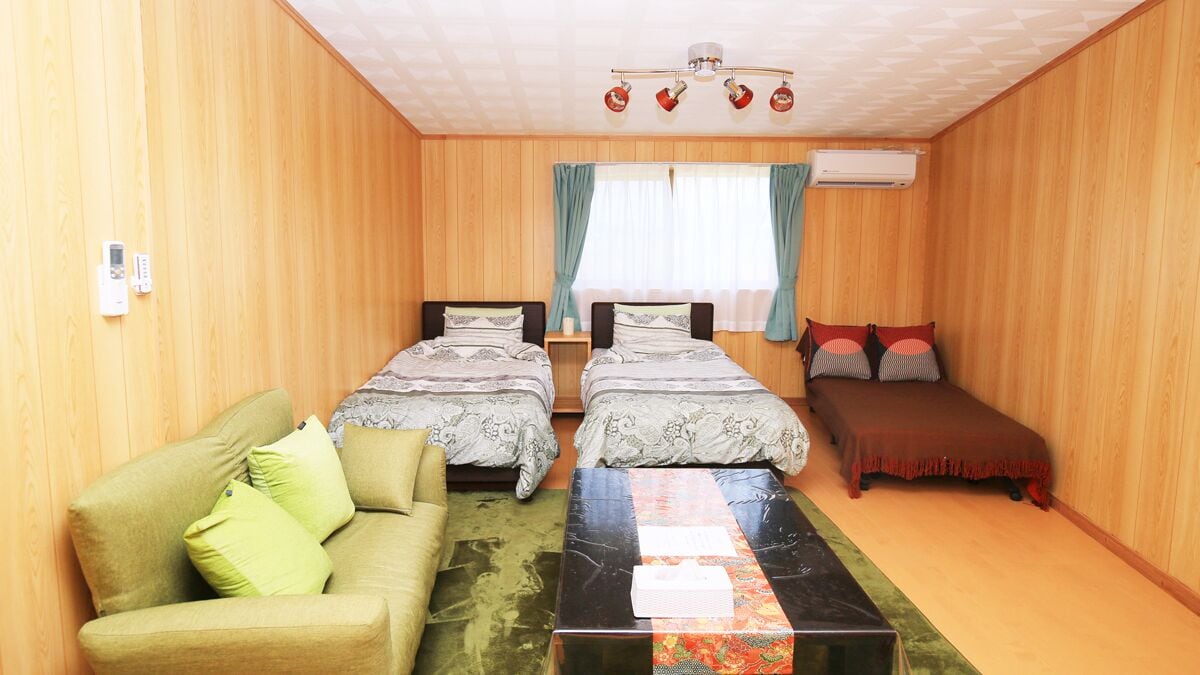 A room with two beds, a sofa, a table, and a ceiling fan.