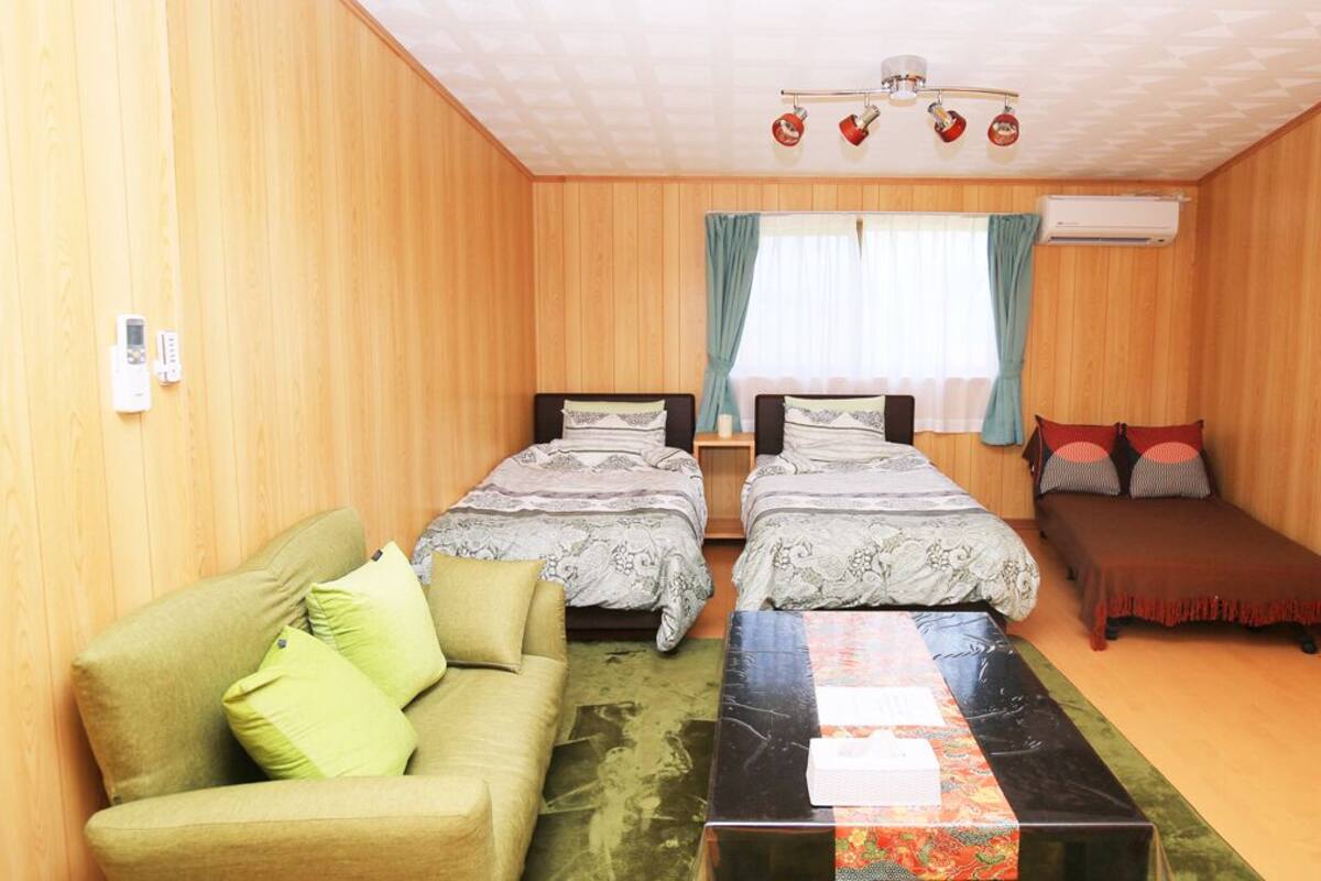 A room with two beds, a sofa, a table, and a ceiling fan.