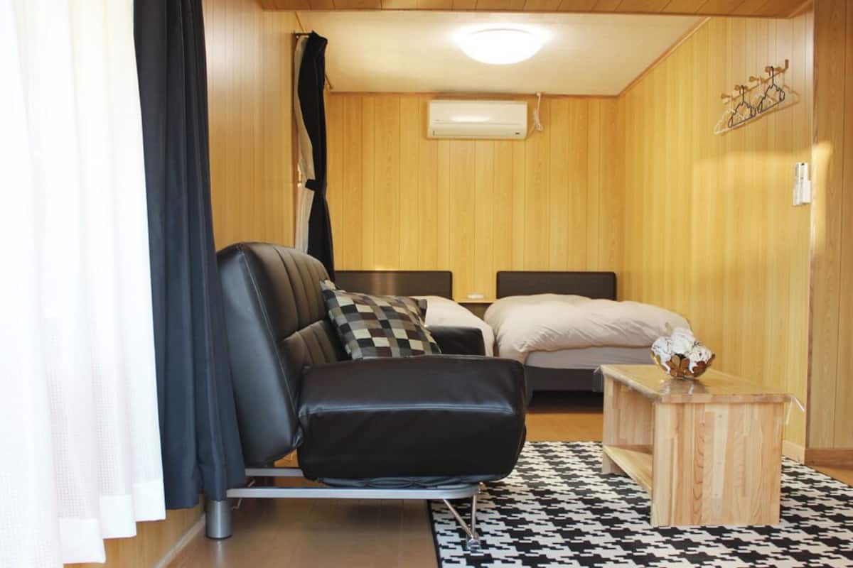 A room with a bed, a chair, a small wooden table, and a patterned rug.