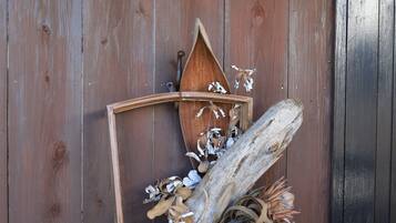 Une porte en bois ornée d’éléments rustiques, notamment une enseigne en bois portant des caractères japonais, une lanterne et divers éléments naturels tels que des feuilles et des branches séchées.