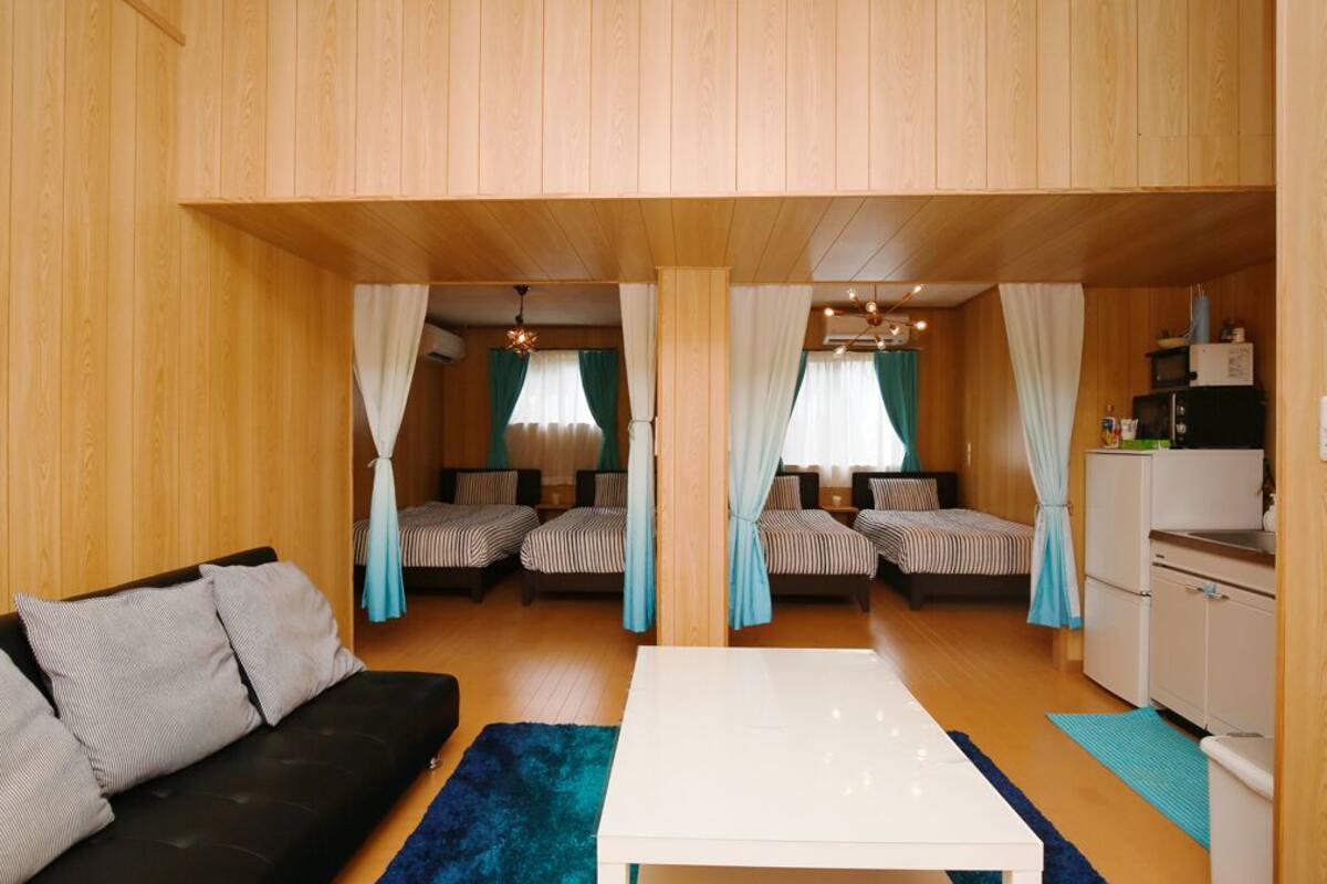 A compact room with two beds, a sofa, a small kitchen area, and a dining table.