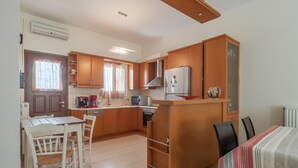 A compact kitchen with wooden cabinets, a refrigerator, a microwave, and a dining area with a table and chairs. - Naxos "Asty" walking distance to everything! (Naxos)