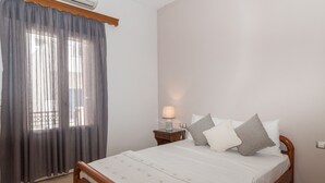 A bedroom with a bed, a nightstand with a lamp, a window with curtains, and a wall-mounted air conditioner. - Naxos "Asty" walking distance to everything! (Naxos)