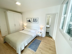 A bedroom with a bed, bedside lamps, a wardrobe, and a bathroom visible through an open door.