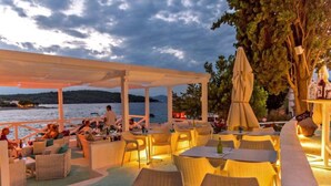 An outdoor dining area with wicker furniture and umbrellas, overlooking a body of water. - Villa Sol - private heated pool & 30m from the sea (Necujam)