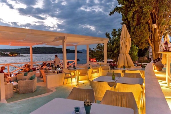An outdoor dining area with wicker furniture and umbrellas, overlooking a body of water.