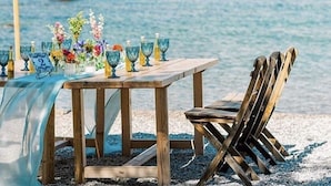 A wooden table with a blue tablecloth and glassware, set against a beach backdrop. - Grande Blue Suites with private bay (Rhodes)