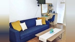 A living room with a blue sofa, a wooden coffee table, and a desk with a chair. - Grande Blue Suites with private bay (Rhodes)