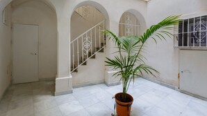 Un espacio interior amplio con pisos de baldosas blancas, paredes blancas y una planta en maceta en el centro.
