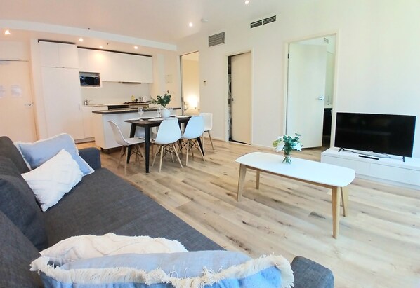 Un salon moderne avec un canapé gris, une table basse et un téléviseur. Il y a également un coin repas avec une table et des chaises.