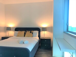 Un lit bien fait, avec deux oreillers, deux lampes de chevet et une petite commode à côté.