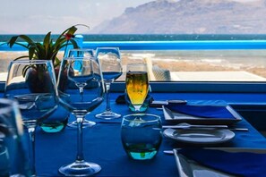 Ein Tisch gedeckt mit Weingläsern und einer Flasche, mit Blick auf einen Strand und das Meer.