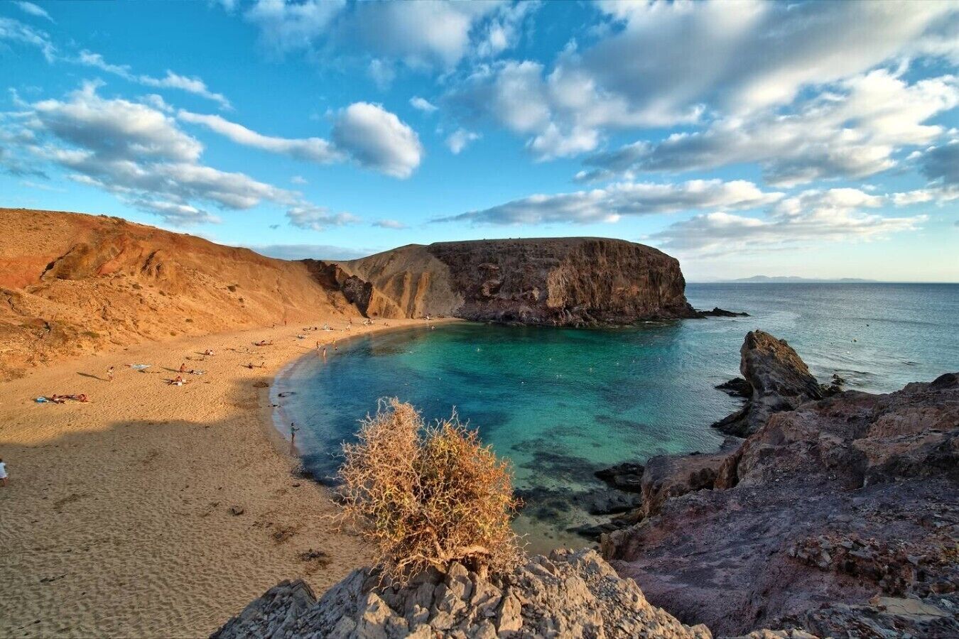 Paisaje costero con una playa arenosa, acantilados rocosos y aguas azules cristalinas.