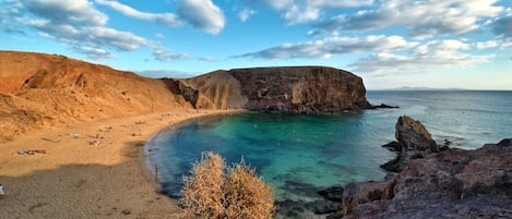 A coastal landscape with a sandy beach, rocky cliffs, and clear blue waters.