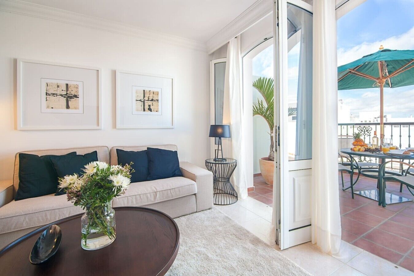 A living room with a sofa, a coffee table with a vase, and a door leading to a balcony with outdoor furniture.