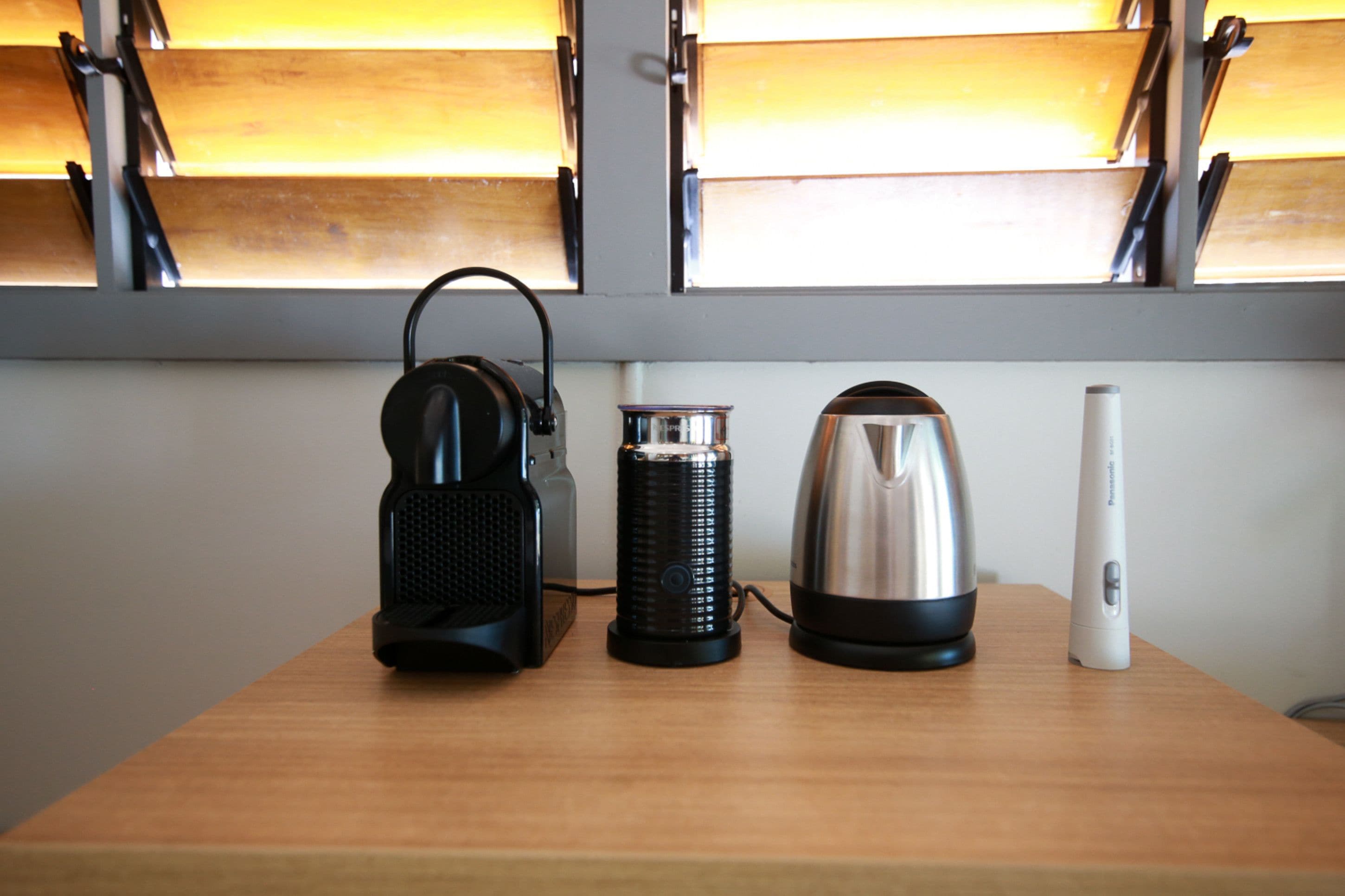 A wooden table with a black speaker, a cylindrical container, a stainless steel kettle, and a white device.