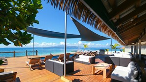 A wooden deck with lounge chairs and sofas, a pool, and a view of the ocean.